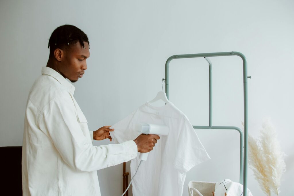 A man uses a steamer to freshen a white shirt on a clothing rack in a minimalist home interior.